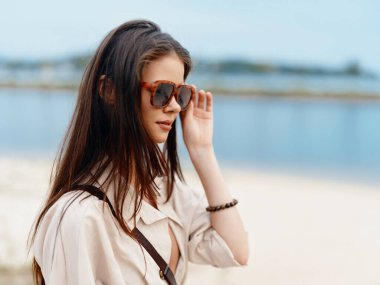 Yaz Güzeli: Sahilde Tatilde Genç Çekici Bir Kadının Portresi, Mavi Okyanus ve Güneşli Gökyüzü Arkaplanına Karşı Güneş Gözlüğü ve Poz Giyiyor