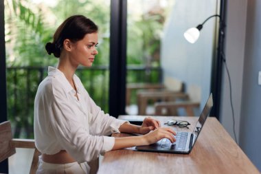 Happy Freelancer İçişleri Bakanlığı 'nda dizüstü bilgisayarda çalışırken gülümseyen kadın rahat iş yerinde oturuyor, bilgisayarında yazıyor, etrafı teknolojik aletlerle çevrili ev ortamında modern bir yaşam tarzını yansıtıyor.,