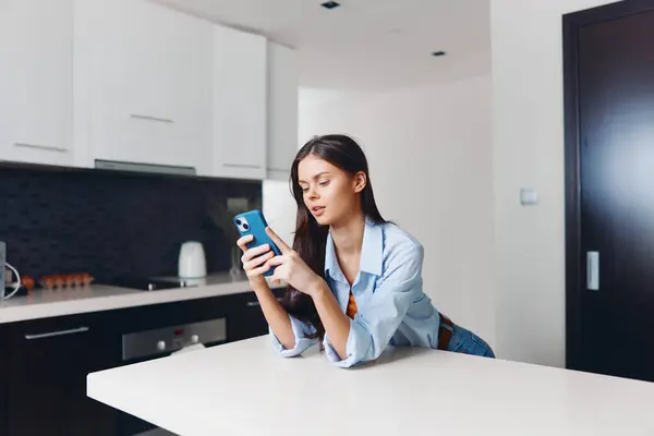 坐在厨房柜台上看手机的女人科技生活观念 — 图库照片