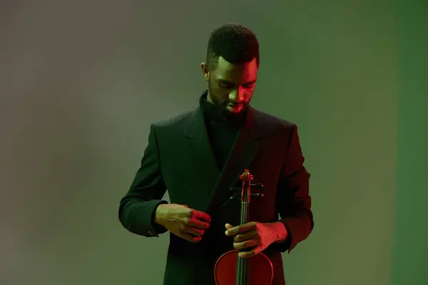輝く緑の背景の前にバイオリンを演奏する黒いスーツの男は エレガントで魅惑的な音楽シーンを作成します ロイヤリティフリーのストック画像