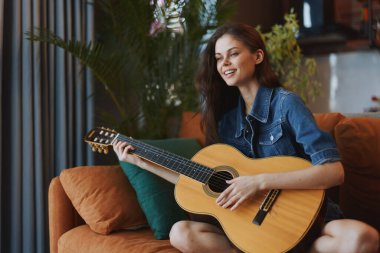 Akustik Gitar Çalan Kadın Sıcak bir atmosferde Bir Pencerenin Önündeki Koltukta Oturuyor