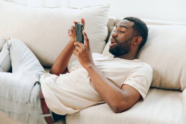 Siyah bir koltukta oturan, elinde bir cep telefonu olan ve mesaj yazan mutlu bir Afrikalı Amerikalı. Rahatlamış ve evde boş zamanlarının tadını çıkarıyor. Sosyal medya aracılığıyla arkadaşlarıyla iletişim kuruyor.