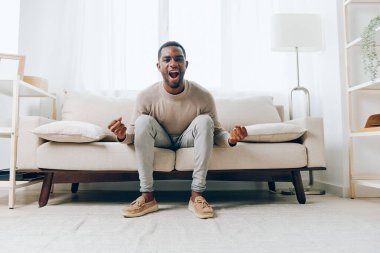 Düşünen Adam Modern Oturma Odasında Konforlu Koltukta Dinleniyor, Gülümsüyor ve Mutlu Afrikalı Amerikalı Genç Yetişkin Rahatlamanın ve Teknolojinin Tadını Çıkartıyor, Dizüstü Bilgisayarı Tutuyor, Evde Tek Başına