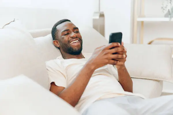 Homem Afro Americano Feliz Sentado Sofá Preto Apartamento Moderno Segurando Imagens De Bancos De Imagens Sem Royalties
