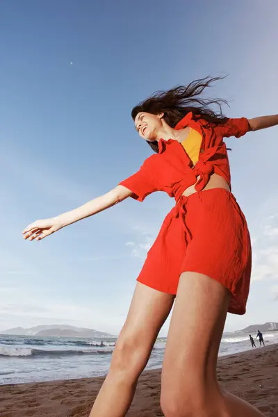 晴れたビーチでジョイと踊る幸せな女性 赤い夏の服の自由と楽しい肖像画 ストック写真