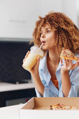 Mutlu genç bayan bir kafede lezzetli bir dilim pizza ve taze bir milkshake yiyor.