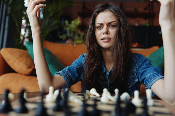 Woman in distress sitting at a table with hands on head, contemplating chess board in front