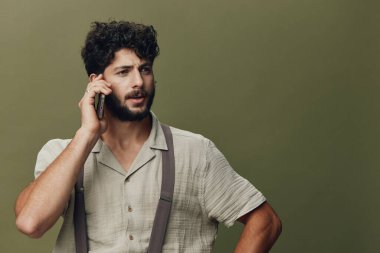 Konuşan genç, münzevi erkek iletişimci adam mutlu jest insanla, neşeli arka planla, mobil telefonla, yetişkin gülüşü sıradan yüz ifadesi portresiyle karşı karşıya.