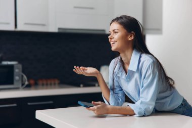 Modern iç mekanlarda mutfak tezgahında oturan kadının önünde cep telefonu var.