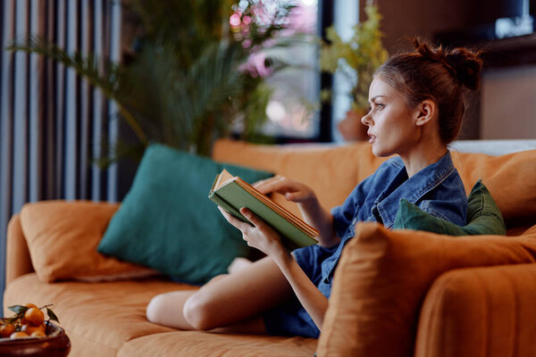 Woman relaxing on couch reading book in front of vase of flowers in cozy home interior setting