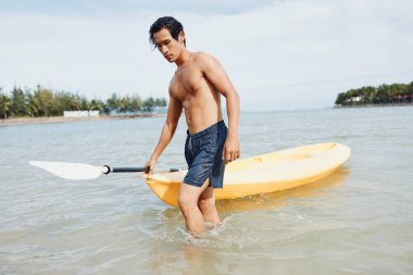 Serene Summer Vibes: Asyalı Adam Tropikal Sahilde Kayak Yapıyor, Sağlıklı ve Aktif Tatilin Tadını Çıkartıyor