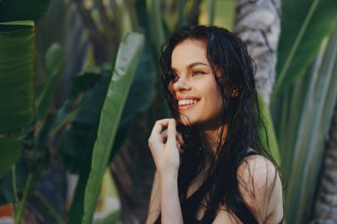 Yeşil Palmiye ağaçlarının önünde duran Islak Saçlı Gülümseyen Tropik Cennet Genç Kadın