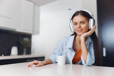 Genç bir kadın mutfaktayken, kulaklıkla müzik dinlemekten zevk alıyor. Rahatlamış ve eğleniyor.