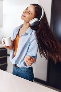 Müzikten ve kulaklıkla kahve içmekten hoşlanan bir kadın. Sabah rahatlaması, favori şarkılar ve sıcak bir içecek.