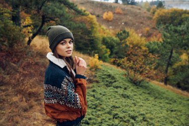 Huzurlu genç bir kadın, arka planda ağaçlar ve dağlar olan güzel bir tarlada doğanın tadını çıkarıyor.