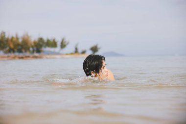 Yüzmek, Sıçramak, Gülümsemek: Tropikal Plaj Tatilinin tadını çıkaran Mutlu Asyalı Adam