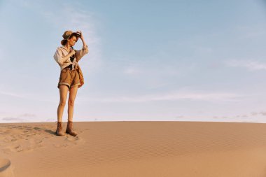 Kum tepeciğinin tepesinde kendine güvenen bir kadın elleri kalçasında uçsuz bucaksız çöl manzarasına bakan