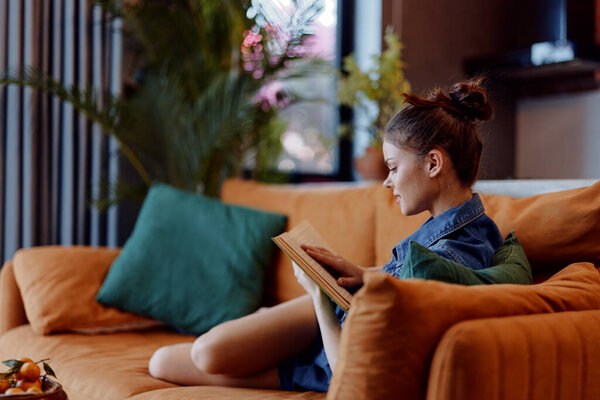 Cozy reading corner with woman sitting on orange couch by window in living room reading book