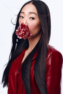 Uzun siyah saçlı, kırmızı ceketli, ağzında çiçekle gizemli bir kadın.