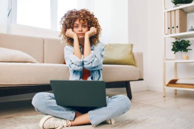 Kanepede oturmak, gülümseyen kadın rahat oturma odasında dizüstü bilgisayarda çalışmak.