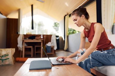 Millennial Yaşam Tarzı 'nda bir kadın İçişleri Bakanlığı' nda bilgisayarını kullanıyor gülümseyen bir öğrenci oturma odasında rahatça oturuyor, evindeki ortamın keyfini çıkarırken onunla çevrimiçi çalışıyor.