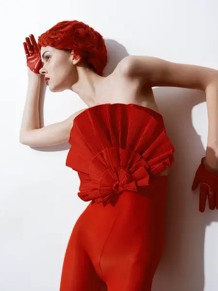 Confident woman in a striking red dress posing with hands on hips against a clean white wall
