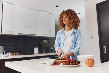 Çekici Afrikalı Amerikalı kadın modern ev mutfağında sağlıklı salata pişiriyor taze sebzelerle, yaşam tarzı konseptiyle.