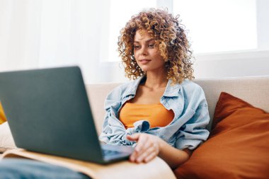 Oturma odasında dizüstü bilgisayarda çalışan gülümseyen kadın.