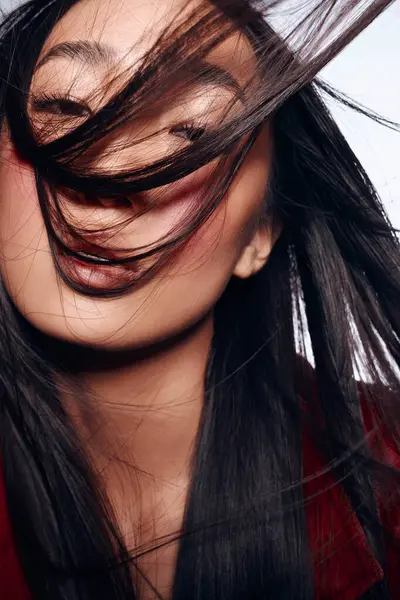 Stock image Stylish woman with long black hair and red jacket blowing hair in the wind