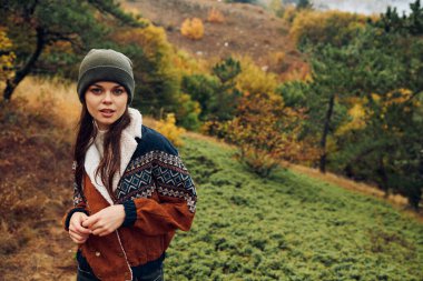 Şık şapkalı ve ceketli şık bir genç kadın ormandaki güzel sonbahar manzarasının tadını çıkarıyor.