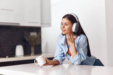 Kadın kulaklıkla müzik dinlerken modern mutfakta, yaşam tarzı konseptinde oturuyor.