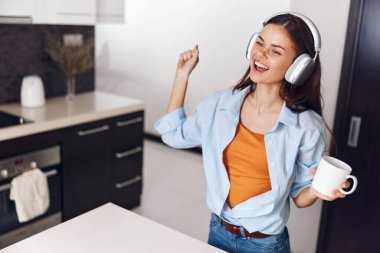 Mutfakta kahve ve müzik eşliğinde kulaklık takan bir kadın rahatlatıcı bir anın tadını çıkarıyor.