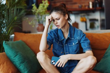 Stresli bir kadın cep telefonuna bakarken koltukta oturuyor.