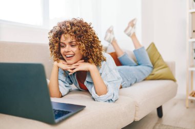 Oturma odasında dizüstü bilgisayarda çalışan gülümseyen kadın.