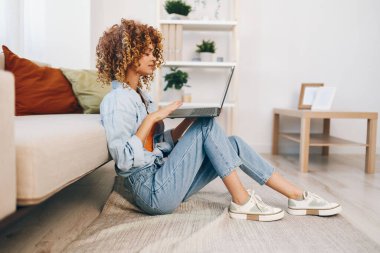 Dizüstü bilgisayarda çalışan gülümseyen bir kadın, rahat bir çalışma odasında serbest çalışmanın keyfini çıkarıyor..