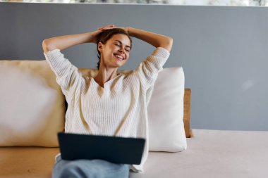 İçişleri Bakanlığı 'ndaki koltukta dizüstü bilgisayar kullanan gülümseyen kadın oturma odasında dinleniyor, koltukta dizüstü bilgisayarla rahatça oturuyor mutlu ve odaklanmış görünüyor.