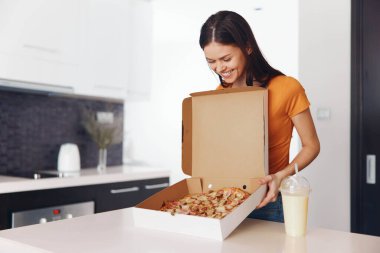Mutfakta pizza kutusunu tutan genç bir kadın.