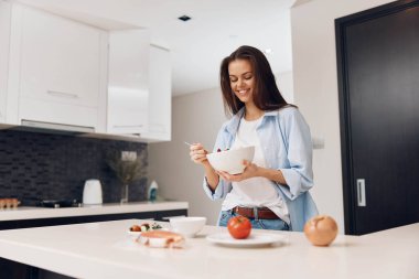 Kadın mutfakta elinde meyve kasesi ve mısır gevreği taze malzemelerle sağlıklı kahvaltı konsepti tutuyor.