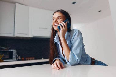 Evdeki çağdaş mutfağın içinde telefonla konuşan mutlu bir kadın.