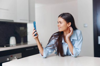 Mutfak tezgahında oturan, telefonu kulağına dayayan, ekrana bakan, göz gezdiren ya da arama yapan bir kadın.