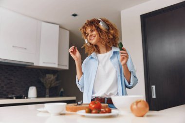 Mutfakta kulaklıkla duran genç bir kadın rahat bir ev ortamında bir kase yemeğin tadını çıkarıyor.