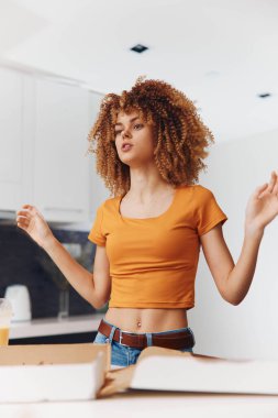 Mutlu kadın, kollarını turuncu gömlekle açıp pizza kutusunun önünde bekleyen lezzetli pizzalardan hoşlanıyor.