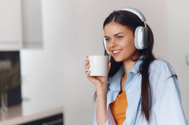 Kadın, mutfaktaki rahat atmosferde kulaklık ve kahve fincanıyla müzik dinlemekten hoşlanıyor.