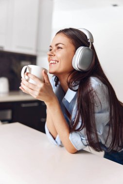 Mutluluktan kahveyi ve müziği seven mutlu bir kadın. Mutfak ortamında kulaklık takıyor.