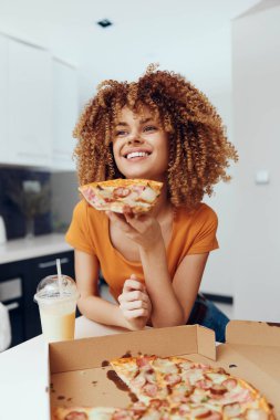 Bir kadın pizza kutusunun önünde pizza yemekten zevk alıyor. Lezzetli bir yemeğin tadını çıkarıyor.