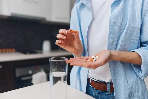 Woman taking medication with a glass of water in the kitchen standing in front of the counter
