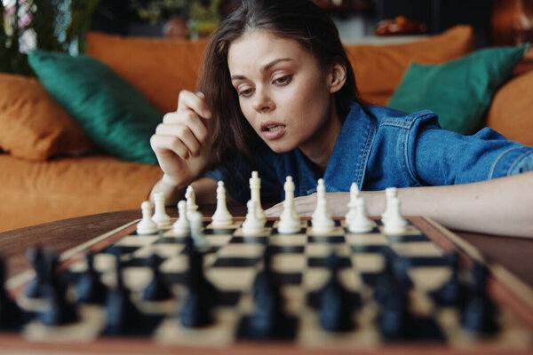 Young woman concentrating while playing a game of chess on a table in a cozy living room setting with a couch in the background