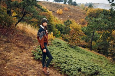 Etrafı sonbahar ağaçları ve doğa güzellikleriyle çevrili sakin bir orman yolunda yürüyüş yapan genç bir kadın.