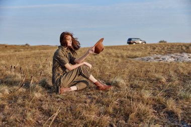 Doğayı ve güzelliği keşfetmek için arka planda şapka ve araba taşıyan bir kadın.