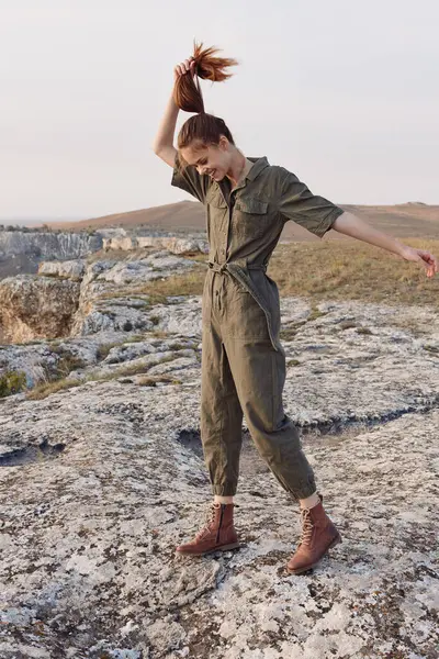 stock image Woman standing on rock with wind blowing hair in green jumpsuit for fashion and outdoor adventure concept